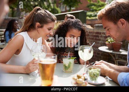 Amici seduti a tavola In Pub giardino guardando il messaggio sul telefono cellulare Foto Stock