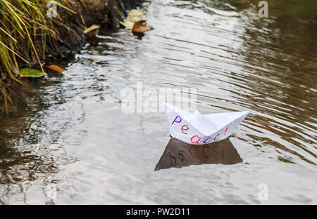 Lonely white paper boat chiamato pace galleggiante su un flusso all'esterno sul cupo giorno di autunno closeup Foto Stock