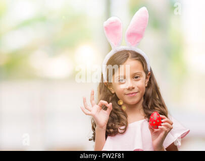 Bruna ragazza ispanica che indossa la pasqua orecchie di coniglio facendo segno ok con le dita, simbolo eccellente Foto Stock