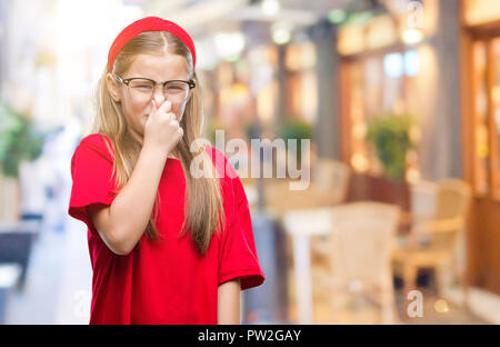 Giovane bella ragazza con gli occhiali su sfondo isolato annusare qualcosa di maleodorante e disgustoso, intollerabile odore, trattenendo il respiro con le dita Foto Stock