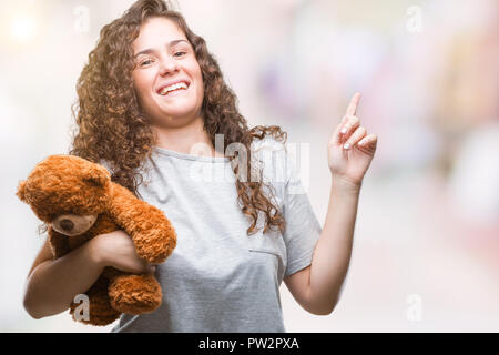 Bruna giovane ragazza con Teddy bear su sfondo isolato molto felice rivolto con la mano e le dita per lato Foto Stock