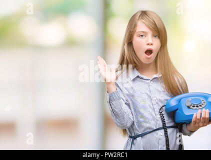 Giovane biondo toddler azienda telefono vintage molto felici ed eccitati, vincitore espressione celebrando la vittoria urlando con un grande sorriso e le mani alzate Foto Stock