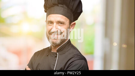 Senior uomo cook, indossando chef hat con bracci incrociati fiducioso e soddisfatto con un grande sorriso naturale di ridere Foto Stock
