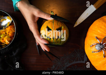 Foto di un uomo con le mani in mano con jack di zucca, coltello seduti al tavolo di legno Foto Stock