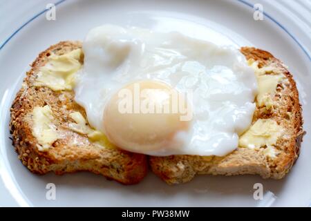 Uovo affogato su brown toast imburrato Foto Stock