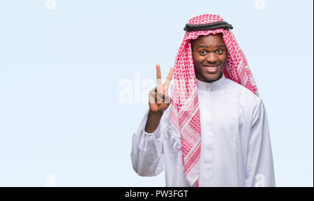 Giovani arabi africano indossando il tradizionale keffiyeh su isolati che mostra sfondo e rivolta verso l'alto con le dita il numero due mentre sorridente fiducioso Foto Stock
