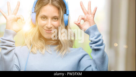 Giovane donna bella ascoltare musica facendo segno ok gesto con entrambe le mani che esprimono la meditazione e relax Foto Stock