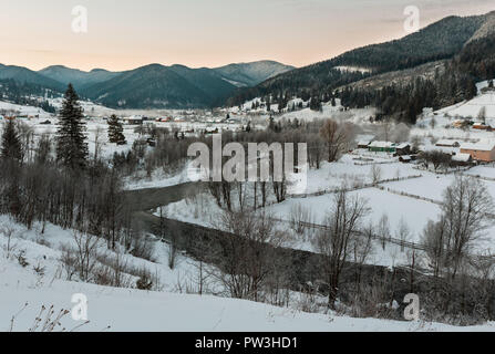 Lo spuntar del giorno mattina inverno tramonto dei Carpazi villaggio di montagna Zelene in nero Cheremosh river valley tra alp. Vista dalla campagna coperta di neve percorso sulla collina Foto Stock