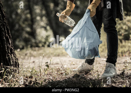 Giovane pupillo indossano jeans e scarpe da ginnastica la raccolta di bottiglie vuote nella foresta Foto Stock