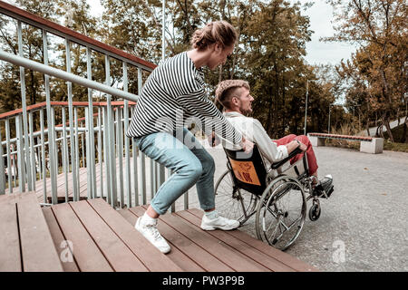 Donna forte aiutando il suo amico e portando la sua sedia a rotelle sulle scale Foto Stock