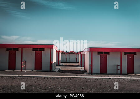 Bella rossa la balneazione case sulla spiaggia sabbiosa. Rifugi vuota su un soleggiato ma moody giorno. Architettura balneare, vernice colorata, maze come labirinto. Da solo. Foto Stock