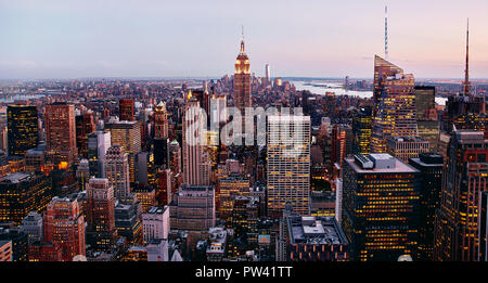Una vista panoramica di Manhattan, New York, NY, gli Stati Uniti. Una piacevole armonia di luci gialle della città e il tramonto rossastro che si riflette sugli edifici degli uffici. Foto Stock