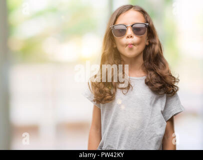 Bruna ragazza ispanica indossando occhiali da sole rendendo il pesce faccia con labbra, pazzo e comico gesto. Espressione divertente. Foto Stock