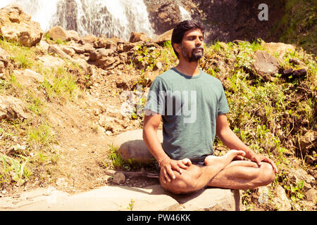 Maschio indiano maestro di Yoga meditazione chiudendo gli occhi su pietre in seduta lotus posano con sfondo naturale Foto Stock