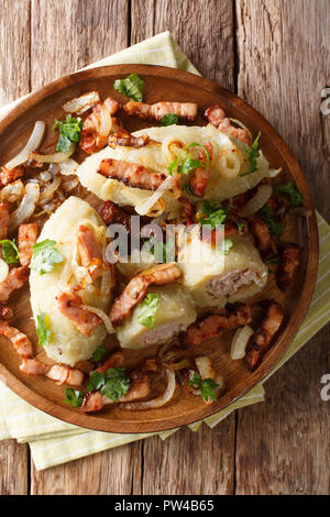 Baltic Cepelinai gnocchetti di patate con ripieno di carne serviti con pancetta e cipolle fritte close-up sul tavolo. Verticale in alto vista da sopra Foto Stock