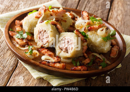 Cucinato al momento Cepelinai gnocchetti di patate con carne macinata servita con pancetta, prezzemolo e cipolle fritte close-up su una piastra sul tavolo orizzontale. Foto Stock