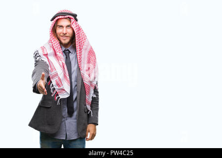 Giovane bello arabian uomo con capelli lunghi che indossa keffiyeh su sfondo isolato sorridente cordiale offrendo stretta di mano come saluto e accogliente. Suc Foto Stock