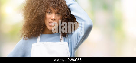 African American shop proprietario donna che indossa un grembiule terrorizzato e nervoso che esprimono l'ansia e panico gesto, sopraffatto Foto Stock