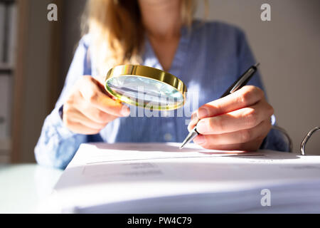 Close-up di una imprenditrice la mano controllo fattura con lente di ingrandimento su scrivania Foto Stock