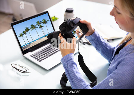 Editor femmina guardando il giovane fotografia nella fotocamera reflex digitale con il laptop sulla scrivania Foto Stock