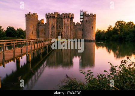 Il Castello di Bodiam, East Sussex, al tramonto con il tramonto del sole e cielo lilla con riflessi nel fossato Foto Stock