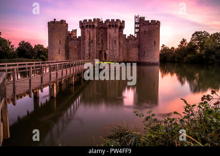 Il Castello di Bodiam, East Sussex, al tramonto con il tramonto del sole e cielo lilla con riflessi nel fossato Foto Stock