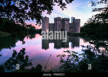 Il Castello di Bodiam, East Sussex, al tramonto con il tramonto del sole e cielo lilla con riflessi nel fossato Foto Stock