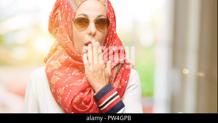 La mezza età araba musulmana donna che indossa il hijab copre bocca in stato di shock, guarda timido, esprimendo il silenzio e confondere i concetti, paura Foto Stock