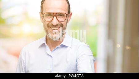 La mezza età l uomo con gli occhiali tiene per mano accogliente nella posa di handshake, esprimendo la fiducia e il concetto di successo, saluto Foto Stock