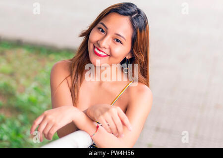 Angolo alto ritratto di sorridente giovane donna in piedi dalla ringhiera in posizione di parcheggio Foto Stock