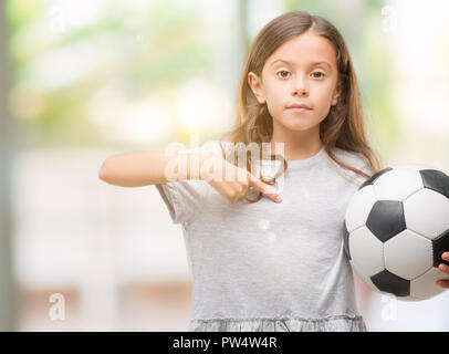 Bruna ragazza ispanica holding soccer football palla con sorpresa faccia puntare il dito a se stesso Foto Stock