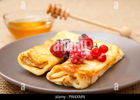 In casa frittelle ripiene di ricotta e guarnita con lamponi congelati e more sulla piastra e miele nella ciotola di vetro con il cucchiaio di legno sul Foto Stock