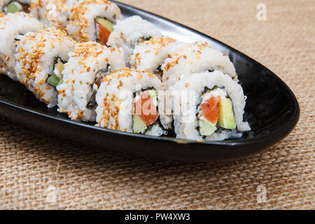 Uramaki sushi rotoli con avocado e pesce rosso sulla piastra in ceramica su un letto di sacco Foto Stock