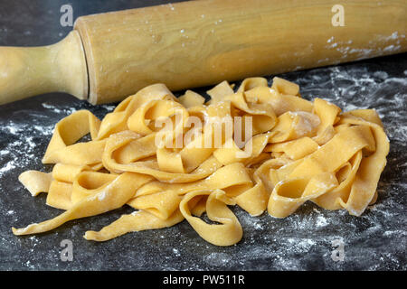 Home tagliatelle fatta chiudere sino a una superficie nera spolverata di farina di legno mattarello in background Foto Stock