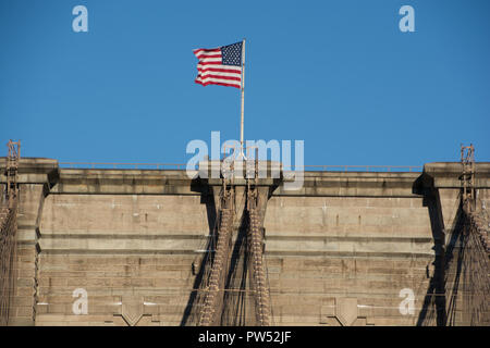 Dettaglio del Ponte di Brooklyn, New York City mostra stomnework, cavi e bandiera americana in un giorno chiaro con il blu del cielo. Foto Stock