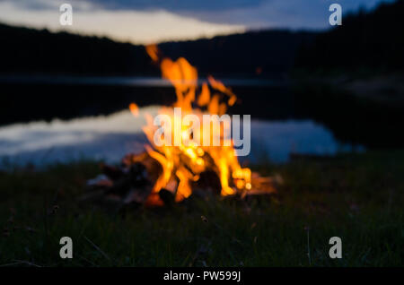 Campfire dopo il tramonto in montagna accanto a un lago Foto Stock
