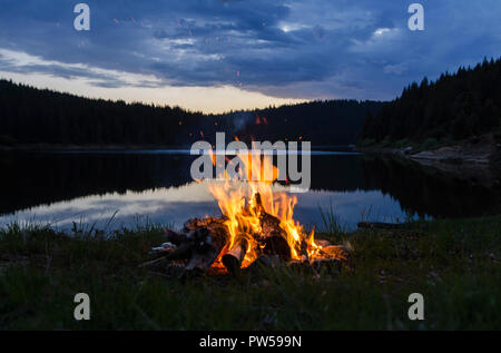 Campfire dopo il tramonto in montagna accanto a un lago Foto Stock