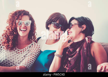 Tre giovani femmine crazy amici avente un sacco di divertimento a casa sul divano. tutti loro con occhiali da sole e laughi e sorrisi. in stretto contatto per il miglior f Foto Stock