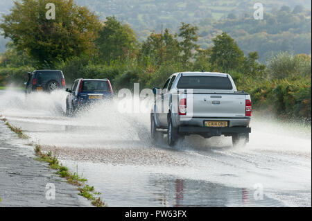 Llangattock, Powys, Wales, Regno Unito. 13 ottobre, 2018. Gli automobilisti guida attraverso l'acqua di allagamento sulla A40 vicino a Crickhowell e Llangattock in Powys, Wales, Regno Unito. Tempesta Callum continua a devastare il Galles del Sud come il fiume Usk burst si tratta di banche come un risultato del massiccio di pioggia torrenziale in Powys inondazioni molti riverside proprietà. © Graham M. Lawrence/Alamy Live News. Foto Stock