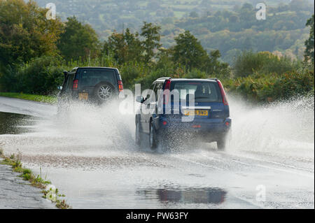 Llangattock, Powys, Wales, Regno Unito. 13 ottobre, 2018. Gli automobilisti guida attraverso l'acqua di allagamento sulla A40 vicino a Crickhowell e Llangattock in Powys, Wales, Regno Unito. Tempesta Callum continua a devastare il Galles del Sud come il fiume Usk burst si tratta di banche come un risultato del massiccio di pioggia torrenziale in Powys inondazioni molti riverside proprietà. © Graham M. Lawrence/Alamy Live News. Foto Stock