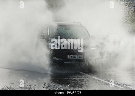 Llangattock, Powys, Wales, Regno Unito. 13 ottobre, 2018. Gli automobilisti guida attraverso l'acqua di allagamento sulla A40 vicino a Crickhowell e Llangattock in Powys, Wales, Regno Unito. Tempesta Callum continua a devastare il Galles del Sud come il fiume Usk burst si tratta di banche come un risultato del massiccio di pioggia torrenziale in Powys inondazioni molti riverside proprietà. © Graham M. Lawrence/Alamy Live News. Foto Stock