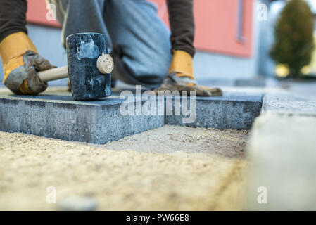 Workman timbratura giù una nuova pavimentazione in mattoni con un mazzuolo. Foto Stock