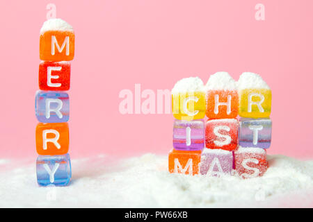 Parole buon Natale fatto di lettere colorate blocchi sul bianco della neve e sfondo rosa. Appartamento laico, vista dall'alto - vacanze inverno, Natale e Anno Nuovo Foto Stock