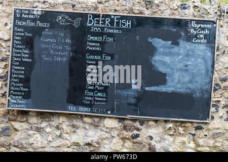 Una bacheca pubblicità una vasta gamma di pesci in vendita in un pescivendolo nel villaggio costiero di birra nel Devon. Foto Stock