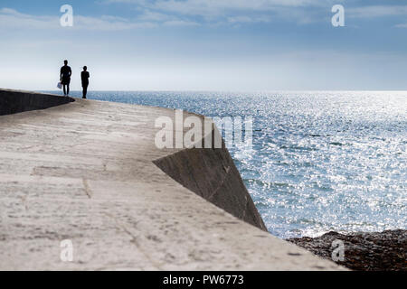 Due persone visto in silhouette camminando lungo il Cobb nella città costiera di Lyme Regis nel Dorset. Foto Stock