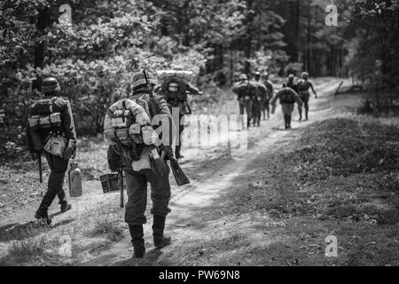 Re-enactors vestito come tedesco soldati di fanteria nella guerra mondiale II marciando a piedi lungo la strada forestale nel giorno d'estate. Foto in bianco e nero e a colori. Foto Stock