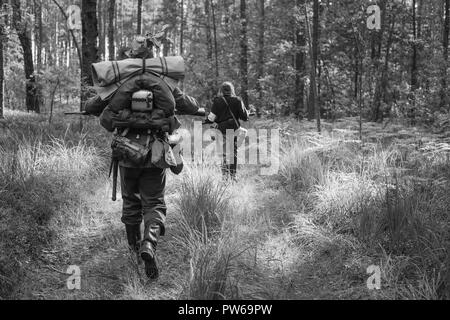 Re-enactors vestito come tedesco soldati di fanteria nella guerra mondiale II marciando a piedi lungo la strada forestale nel giorno d'estate. Foto in bianco e nero e a colori. Foto Stock