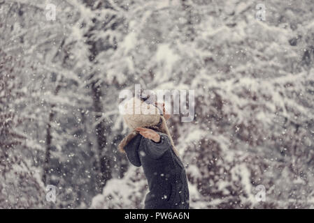 Effetto retrò sbiadito e tonica immagine di una donna che celebra l'inverno in piedi all'aperto in caduta di neve con le braccia esteso. Foto Stock