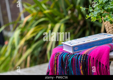 Coperta di tartan libro aperto su un tavolo giardino all'aperto mock up flatlay, timeout concetto, hygge, lo stile di vita facile vivere, miglior vita rilassato rilassante sfocato Foto Stock