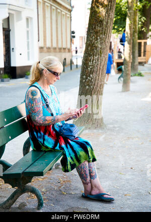 Donna seduta da sola su una panchina verde pubblica presso la banca canale, preparandosi a scrivere sul telefono cellulare. Città di Brugge, Belgio. Foto Stock